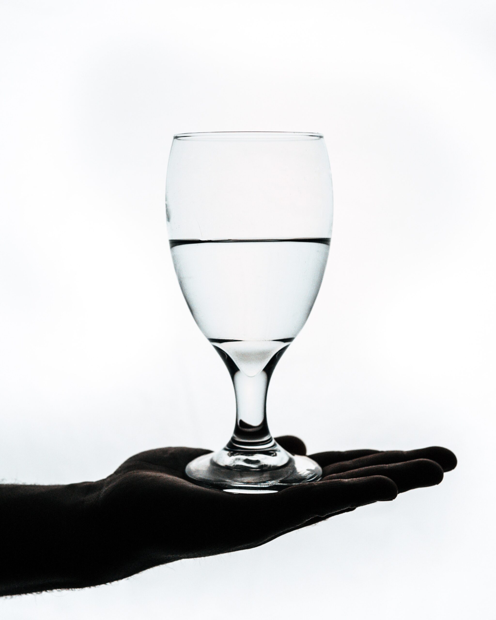 A wine glass full of water is held in the palm of a hand.