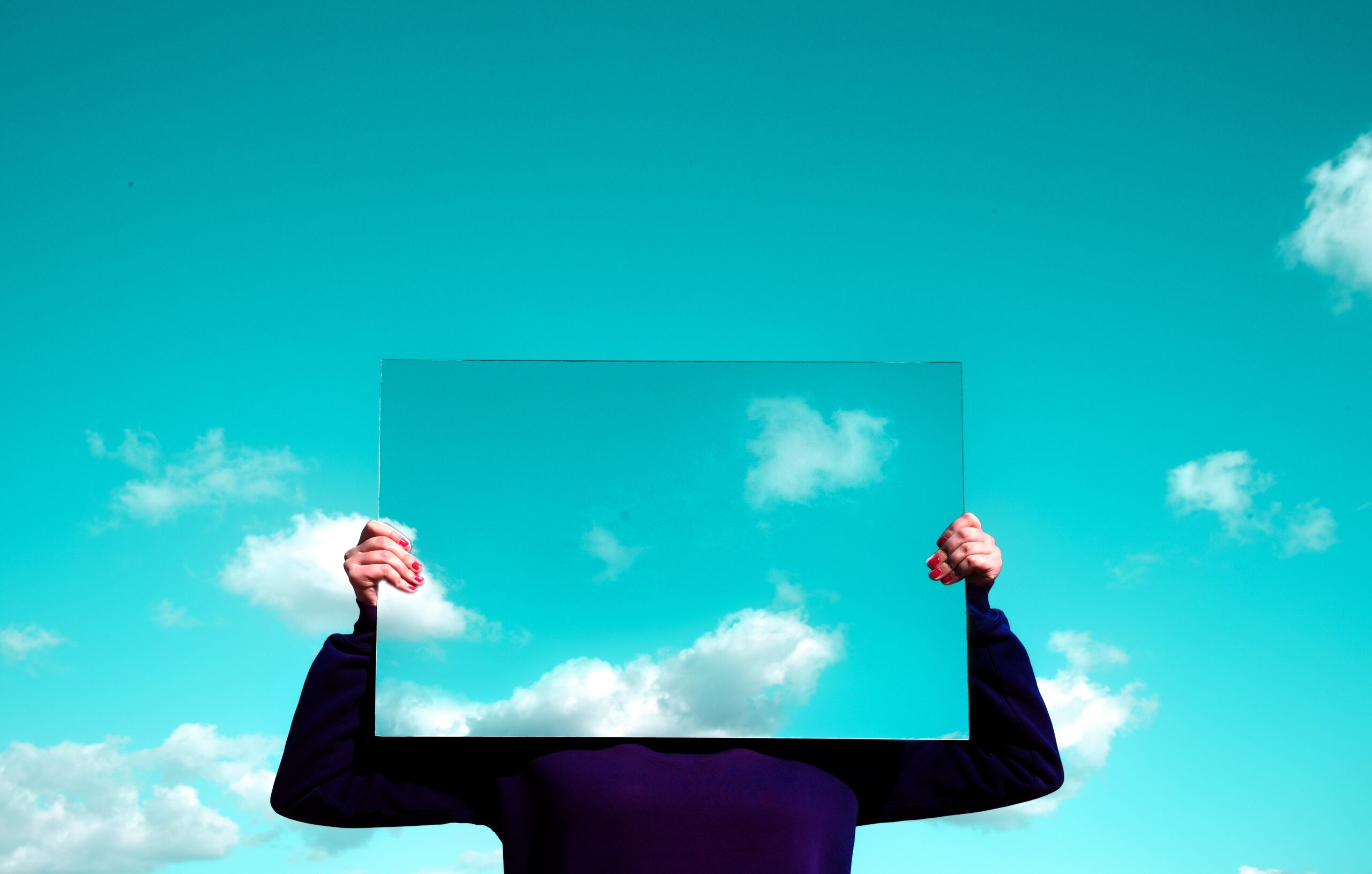 A person holding a mirror that has a reflection of the sky